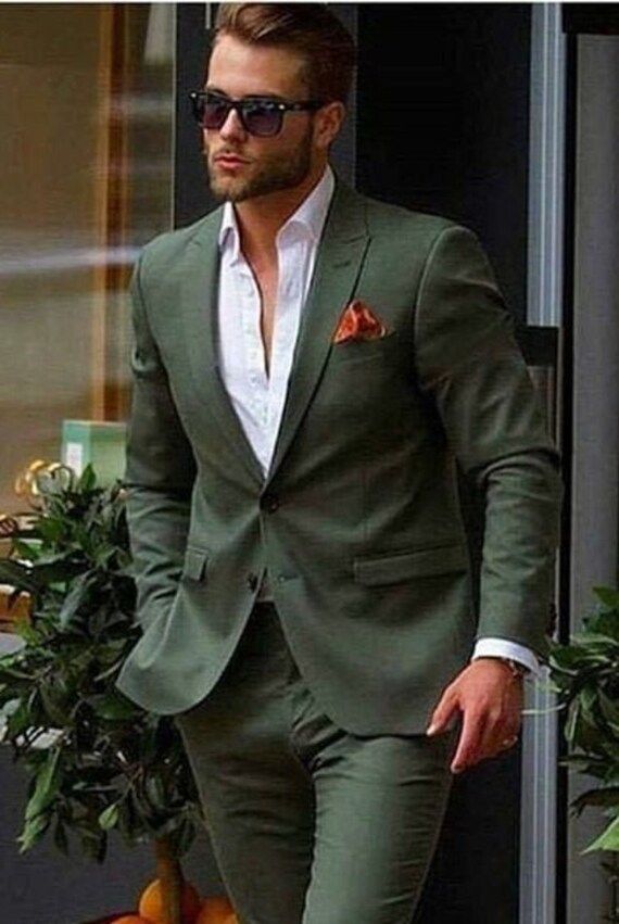 a man in a green suit and sunglasses is walking down the street with his hands in his pockets