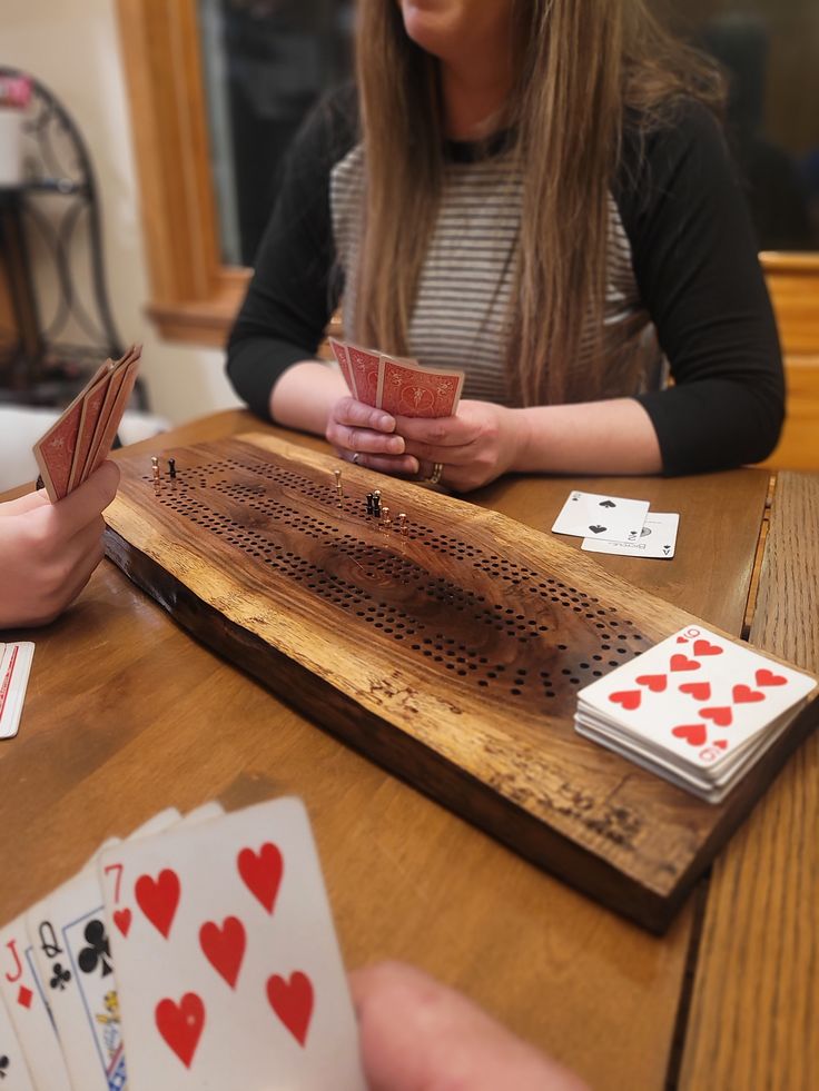 two women sitting at a table with playing cards in front of them and one holding a cup