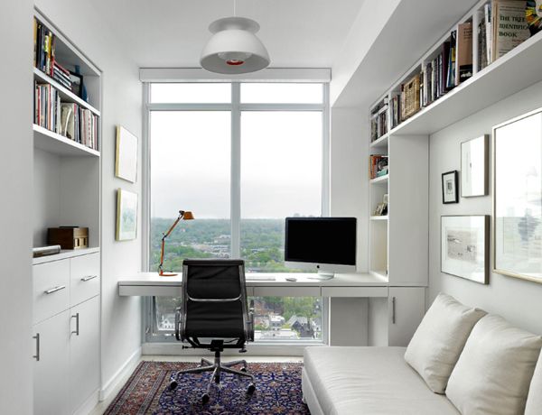 a room with a couch, desk and bookshelves on the wall in front of a large window