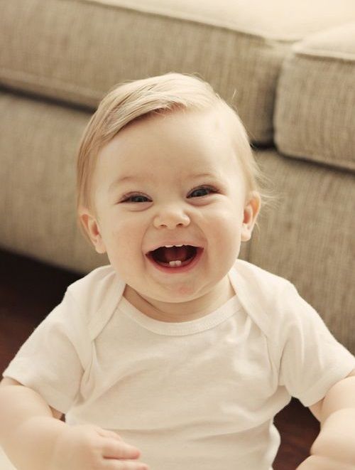 a smiling baby sitting on the floor in front of a couch