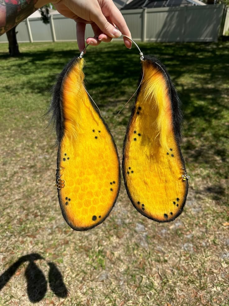 someone is holding up two yellow and black pieces of animal fur that have holes in them