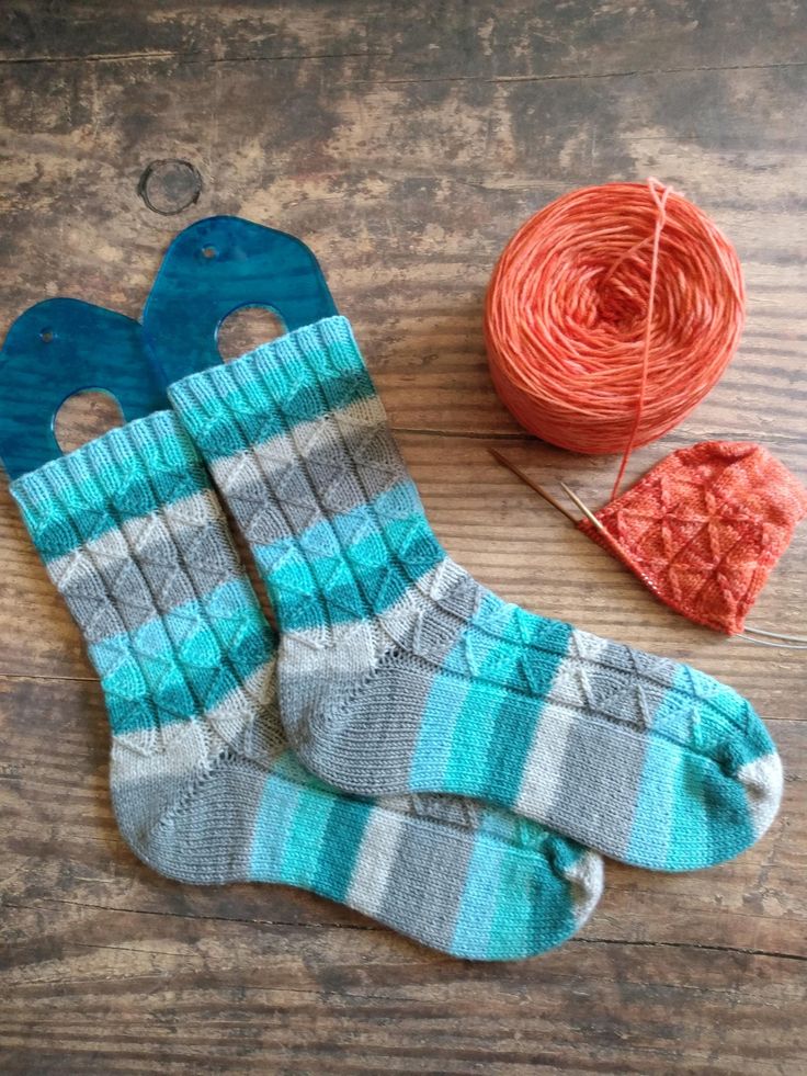 two pairs of socks sitting on top of a wooden floor next to a ball of yarn