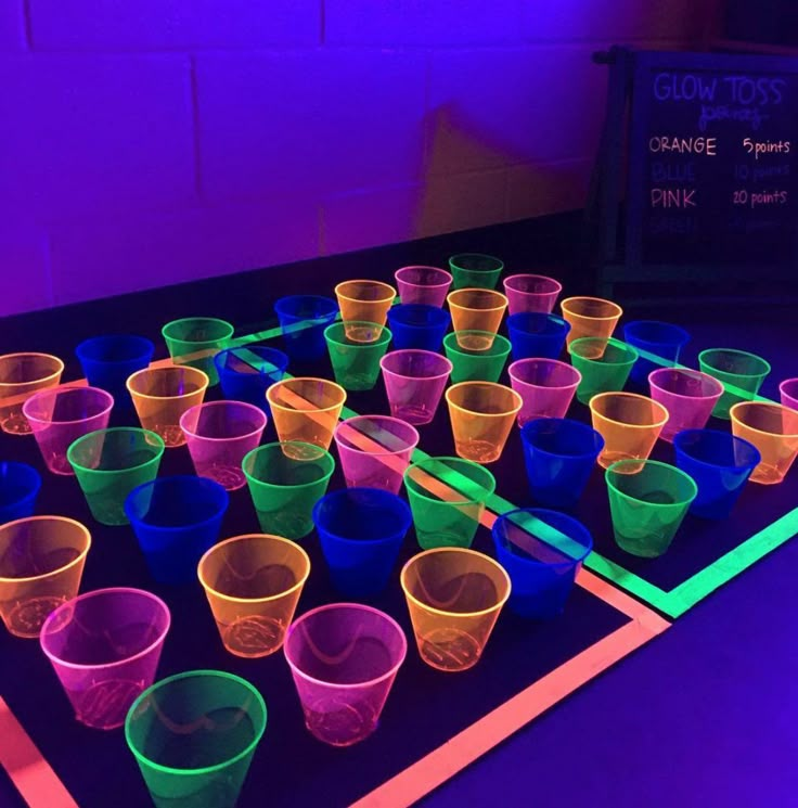 plastic cups are lined up on a table with glow sticks in the middle and purple lighting behind them