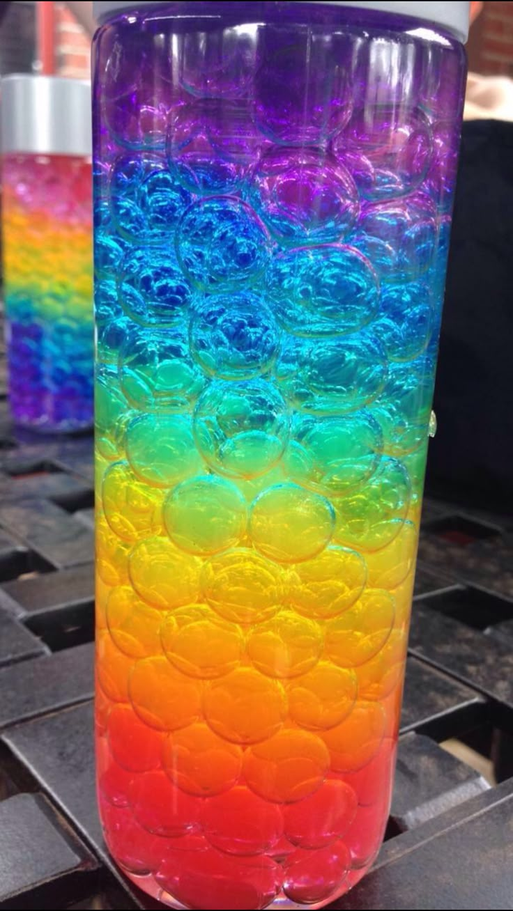 a rainbow colored glass sitting on top of a metal table next to another glass with bubbles in it