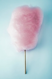 a pink cotton candy lollipop on a stick against a light blue background with copy space