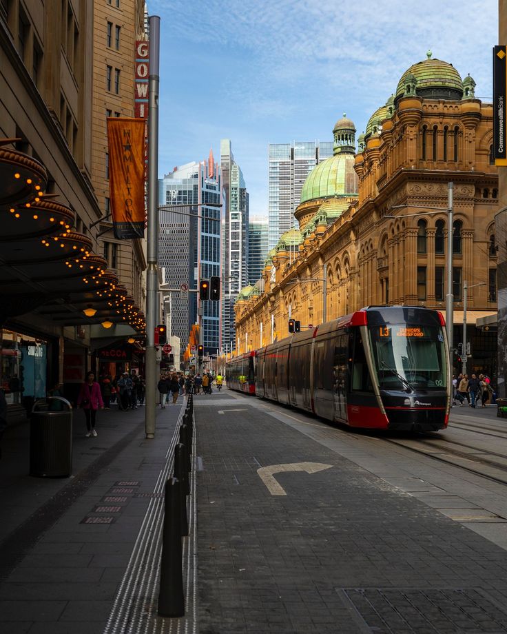 a red and black train traveling down tracks next to tall buildings on a city street