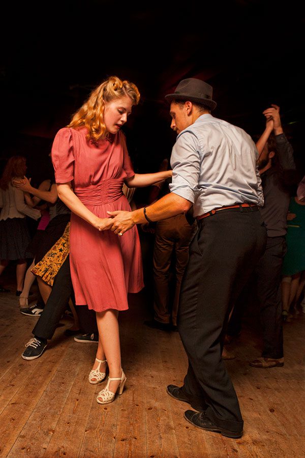 a man and woman dancing on a wooden floor in a dark room with other people