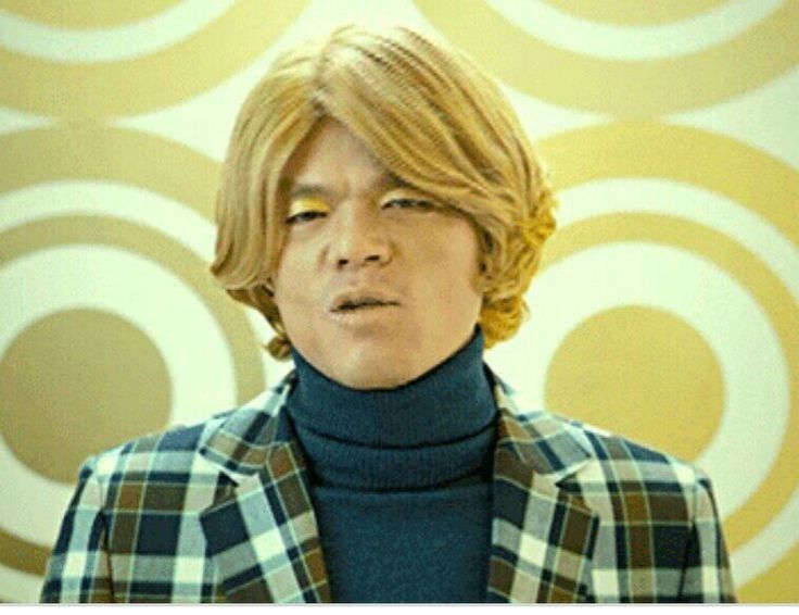 a man with blonde hair wearing a blue turtle neck sweater and plaid blazer jacket