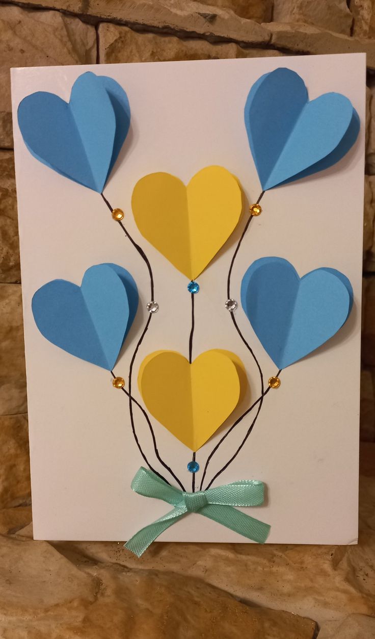 a card with blue, yellow and white balloons on it's side in the shape of hearts