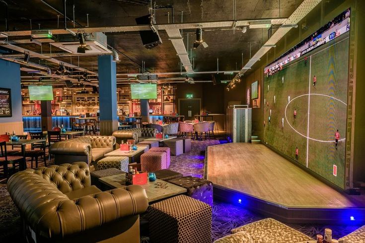 a sports themed bar with couches, tables and chairs in front of a large screen