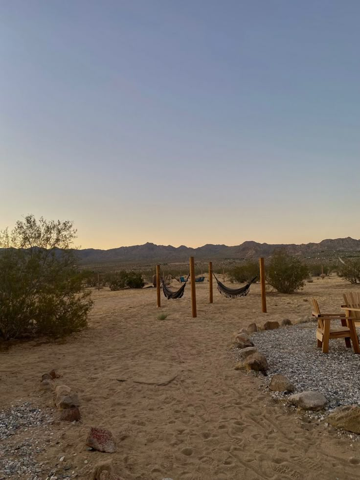 two wooden benches sitting on top of a sandy beach next to hammock chairs