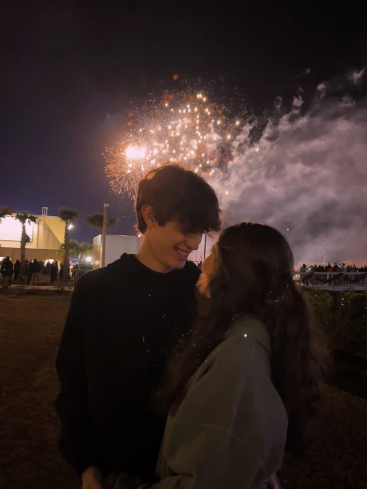 two people standing next to each other with fireworks in the background