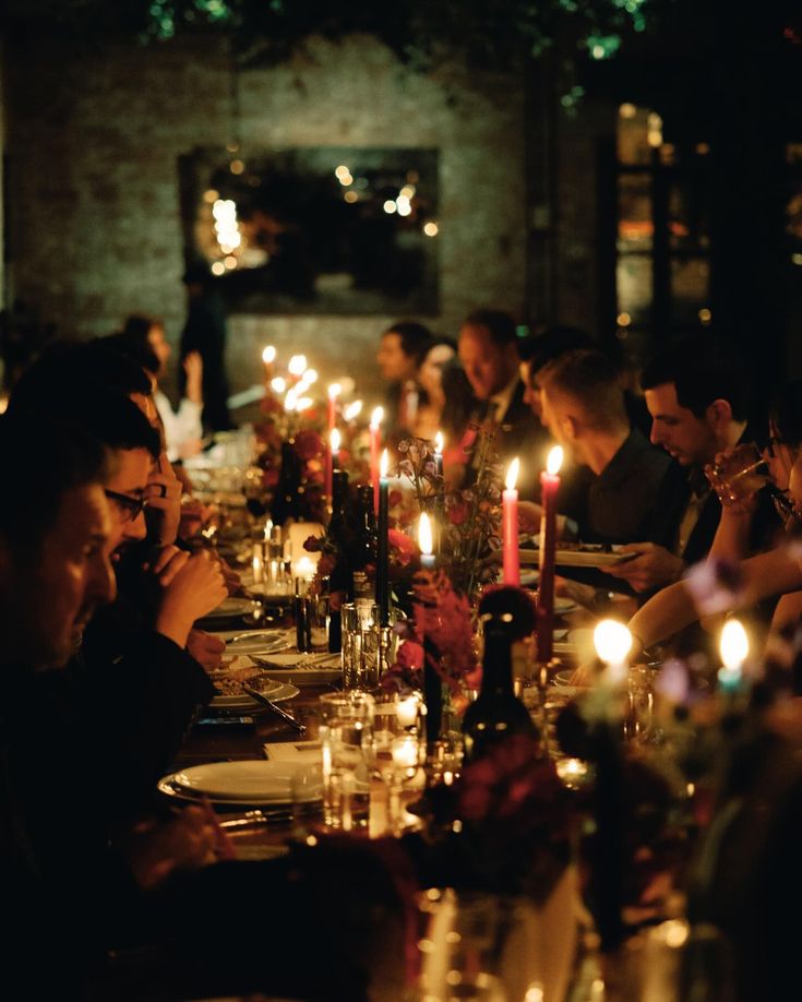 a group of people sitting around a dinner table with candles in the middle of them