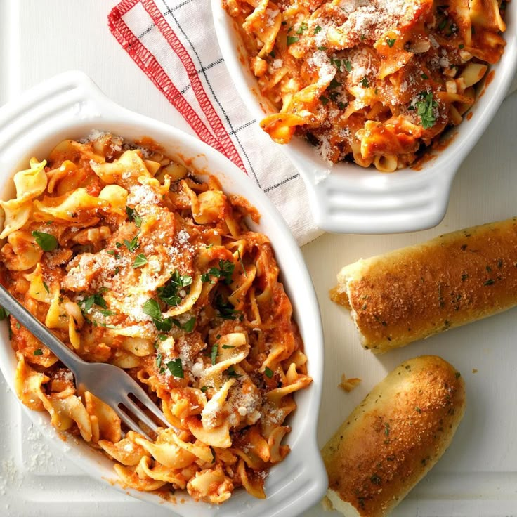 two bowls of pasta with bread on the side