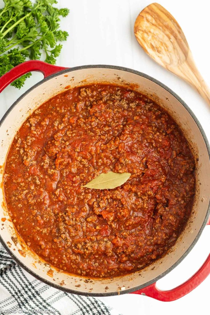 a red pot filled with chili sauce and parsley on top of a white table