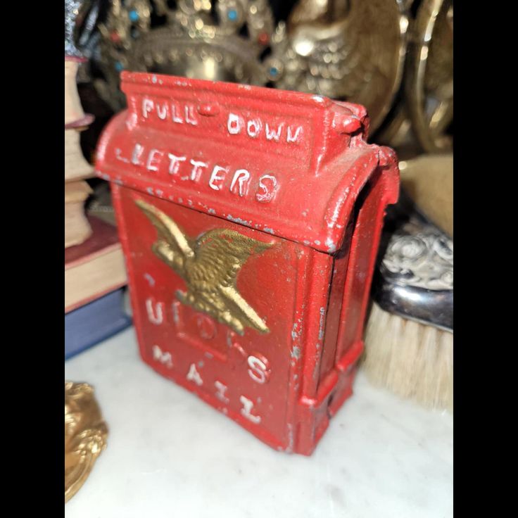 a red metal mailbox sitting on top of a table next to books and other items