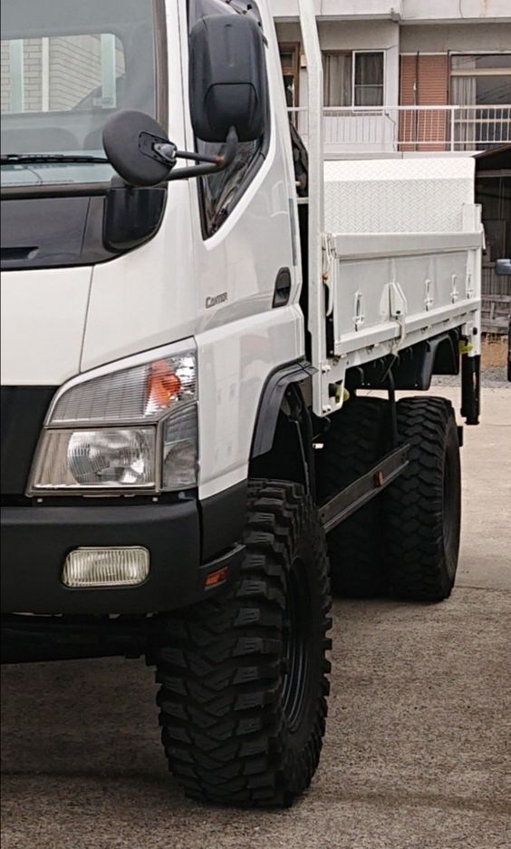 a white dump truck parked in front of a building with large tires on it's sides