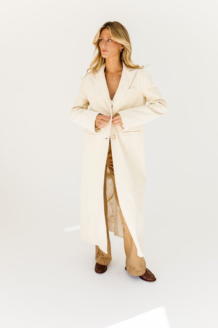 a fresh take on the oversized blazer, this cream trench coat is a must-have for business casual baddies. it has a relaxed longline silhouette, luxe working buttons, + is made with a thick cotton material (so it will actually keep you warm). the perfect spring // winter coat to elevate your casual fits or embellish your formal ones. natural // lapel collar, buttons, pockets, cuffed sleeves, corduroy paired with our charlotte wrap top + kenny cargo pants + hardi slingback penny loafers model is 5' Chic Cotton Outerwear With Hidden Button Closure, Chic Notch Lapel Outerwear For Everyday, Chic Everyday Outerwear With Notch Lapel, Chic Everyday Blazer With Notch Lapel, Chic Oversized Long Coat Blazer, Cream Single Breasted Outerwear For Business Casual, Cream Single-breasted Outerwear For Business Casual, Cream Outerwear With Double Button And Notch Lapel, Chic Long Cotton Coat