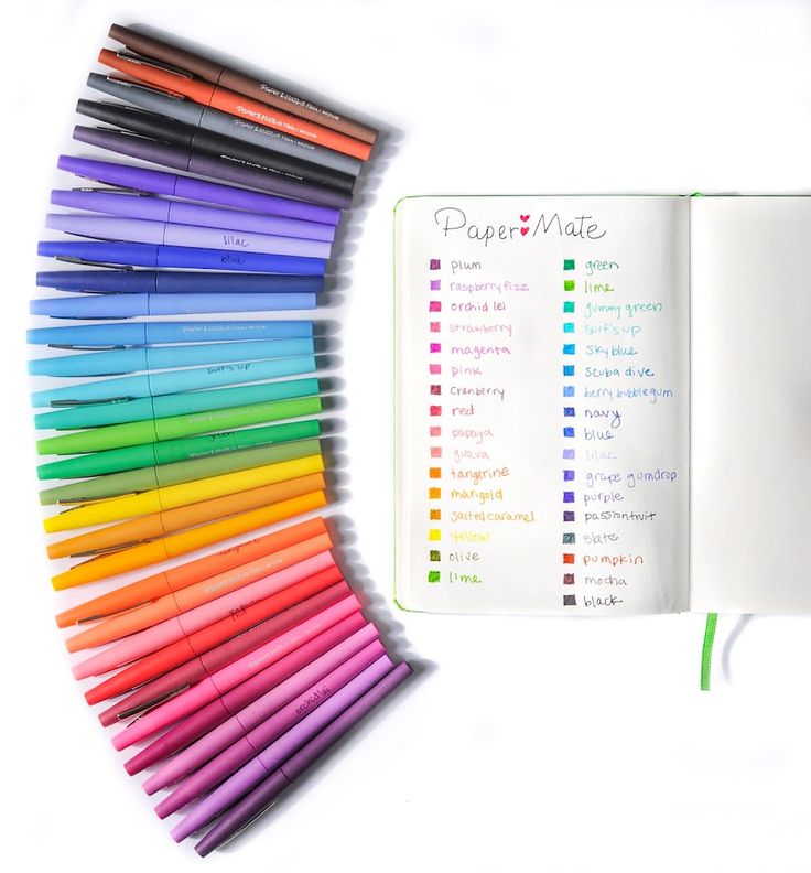 an open notebook with colored markers next to it on a white surface, surrounded by rainbow pens