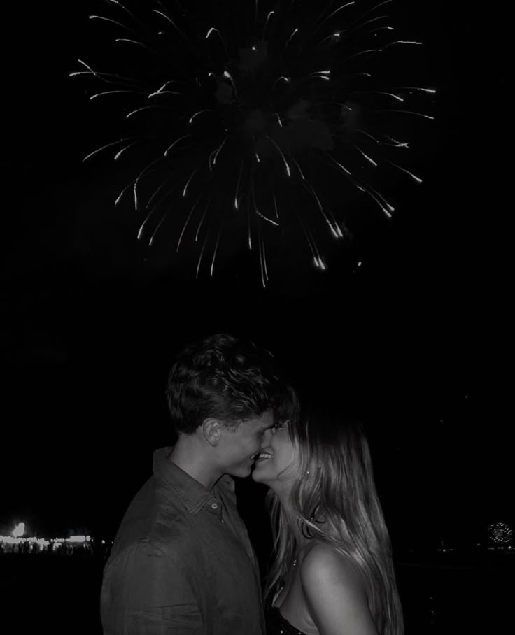 a man and woman standing next to each other with fireworks in the sky behind them