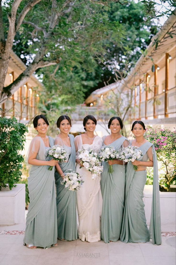 a group of women standing next to each other in front of trees and bushes holding bouquets