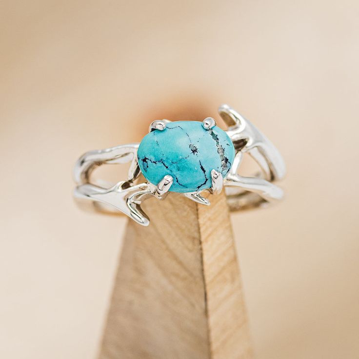 a turquoise stone ring sitting on top of a wooden stand in front of a beige background