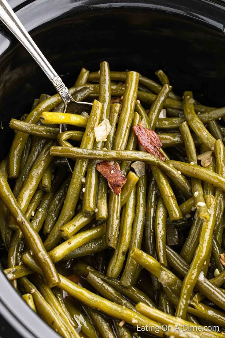 cooked green beans in a crock pot with tongs