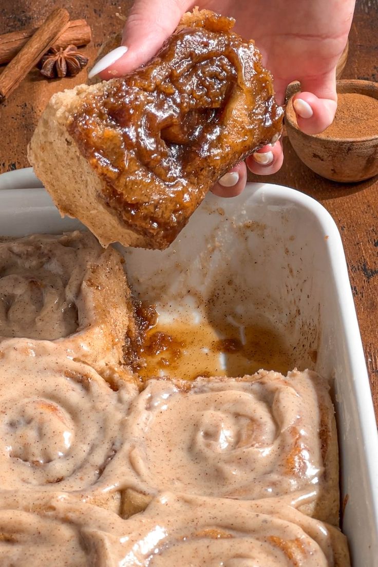 a person dipping cinnamon rolls into a baking dish