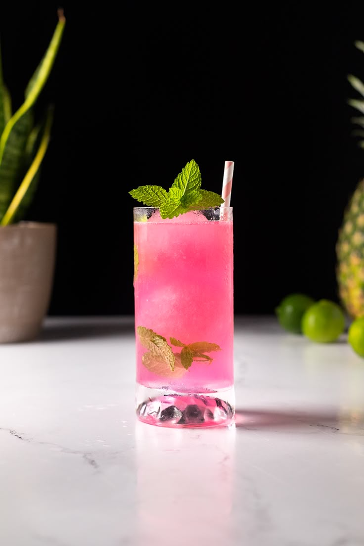 a pink drink sitting on top of a table next to a potted pineapple