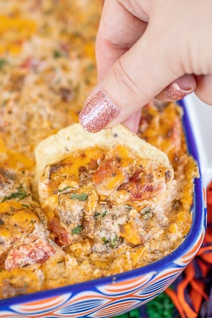 a hand dipping a tortilla chip into a casserole in a blue dish