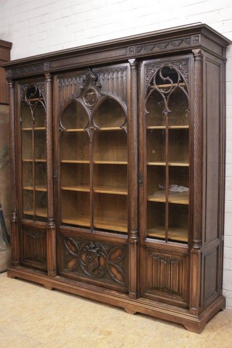 an old wooden bookcase with glass doors and ornate carvings on the front, sitting against a white brick wall