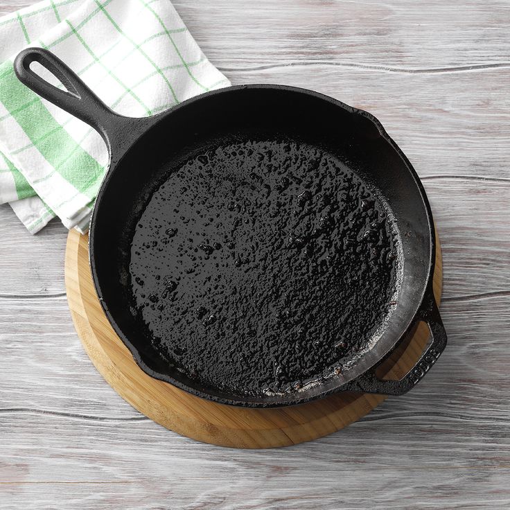 a cast iron skillet filled with black powder on top of a wooden table next to a green and white towel