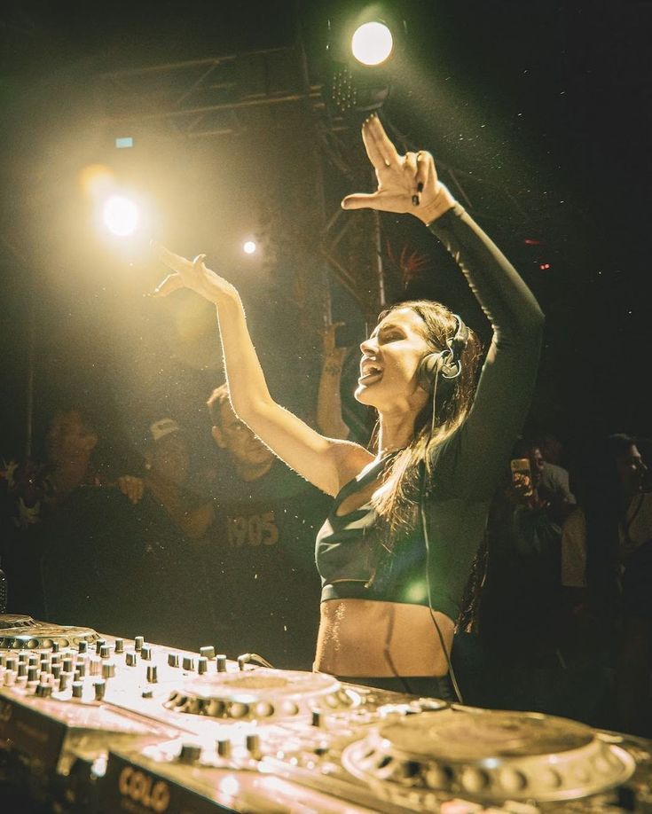 a woman standing in front of a dj's mixer at a party with her hands up