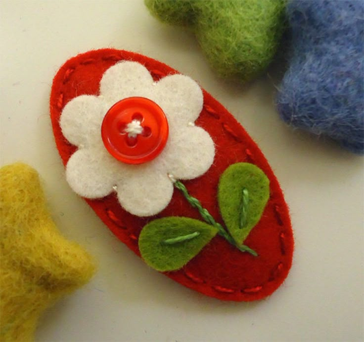 three felt flower brooches with leaves and one button on them, sitting next to each other