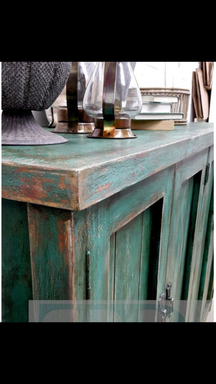 an old green wooden cabinet with glass vases on top and other items in the background