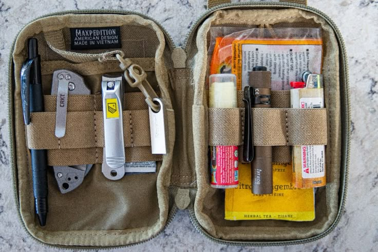 the contents of an outdoor survival kit are neatly packed in a pouch on a marble countertop