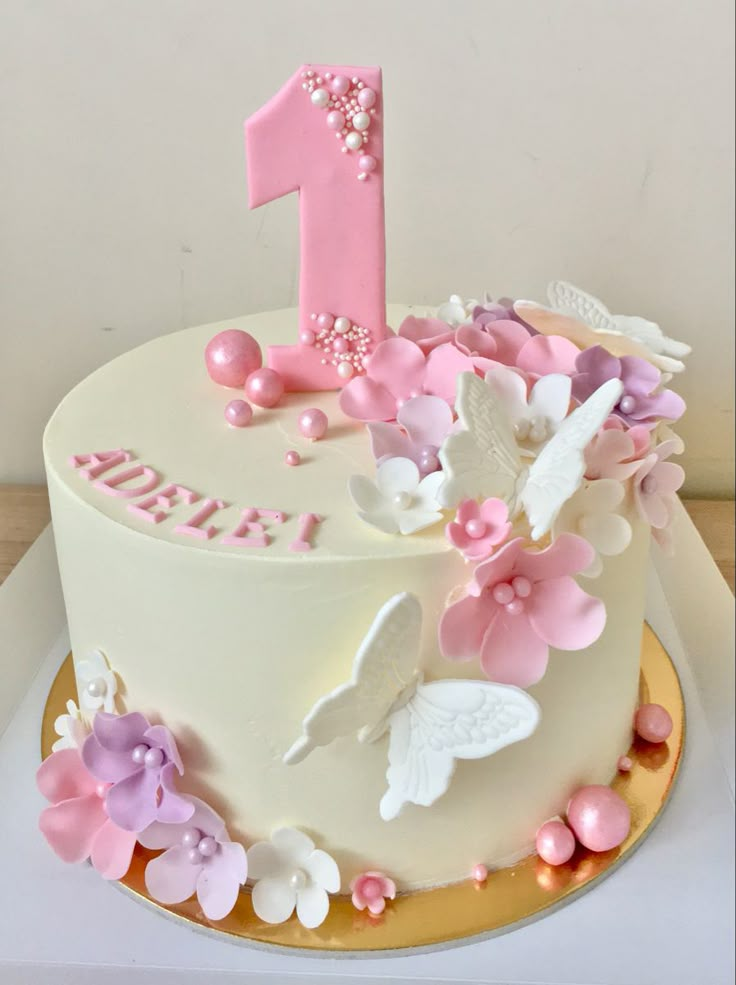 a white cake with pink and purple flowers on the top is decorated with a number one