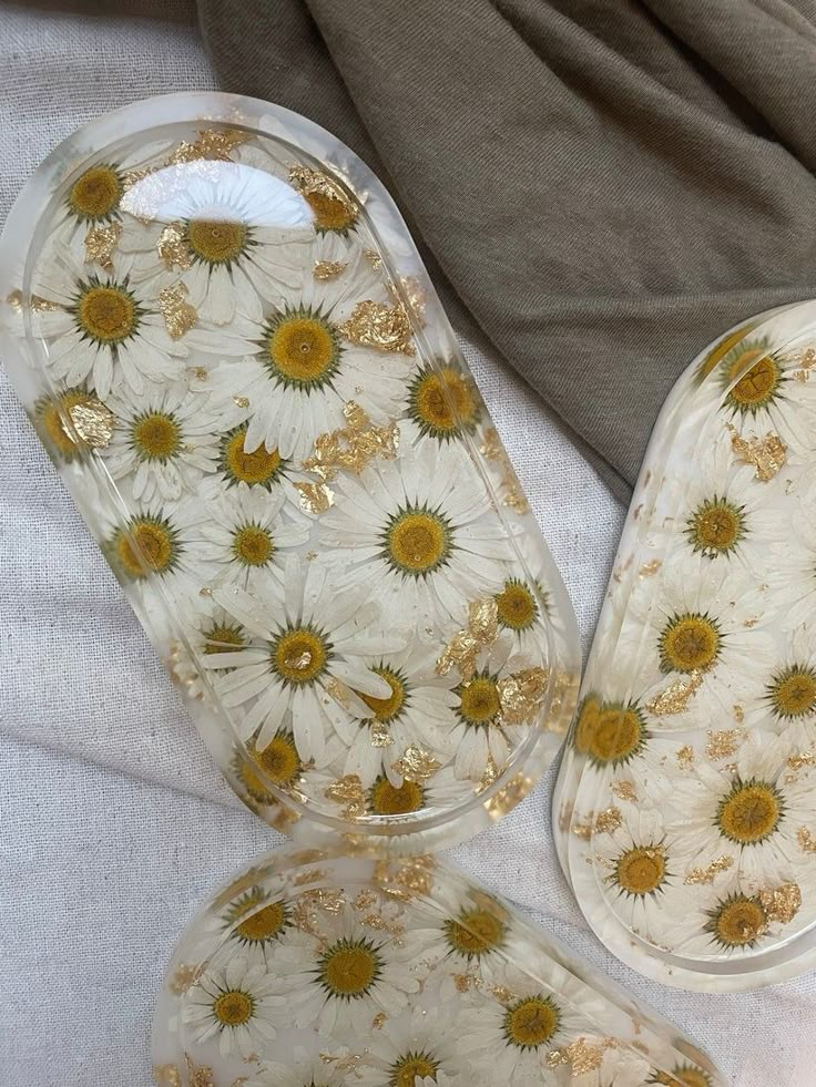 three glass dishes with yellow and white flowers on them sitting on a bed next to each other