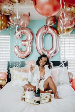 a woman sitting on top of a bed holding a bottle of champagne in front of balloons