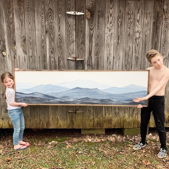 two young children standing next to a painting on the side of a wooden fenced in area