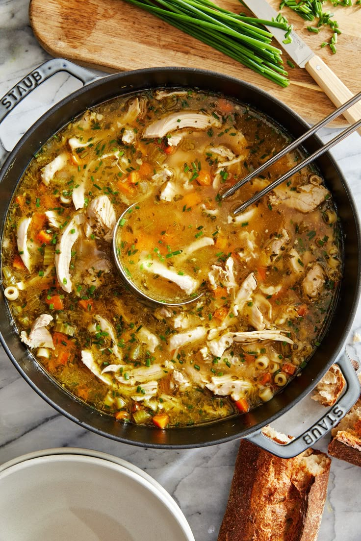 a pan filled with chicken and vegetable soup on top of a table next to bread