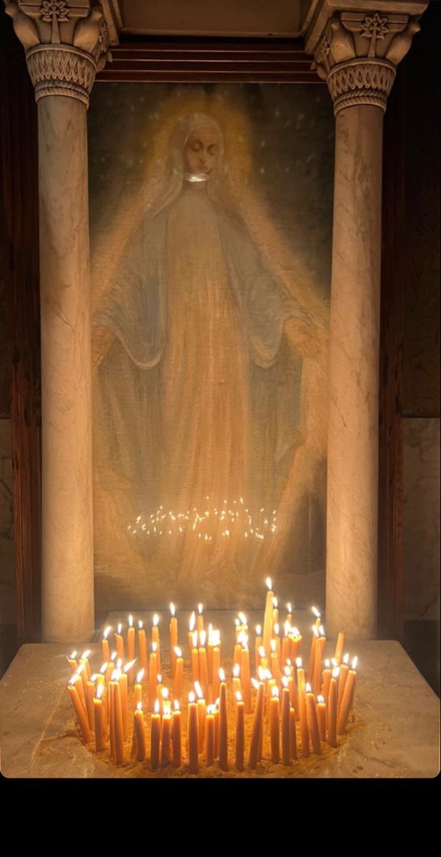 candles are arranged in front of a statue with the image of jesus on it, surrounded by pillars