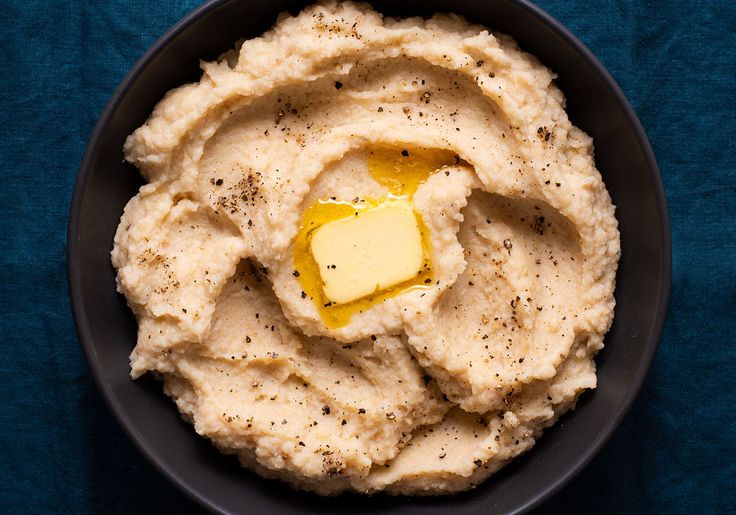 mashed potatoes with butter in a black bowl on a blue tablecloth, top view