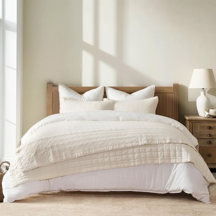 a bed with white linens and pillows in a neutral room next to a window