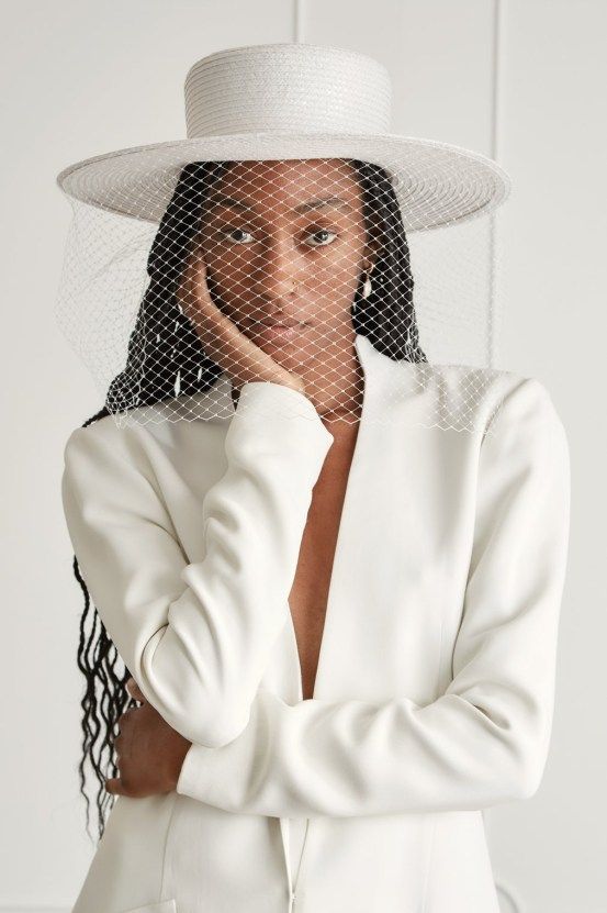 a woman wearing a white hat and jacket with veil over her face, posing for the camera