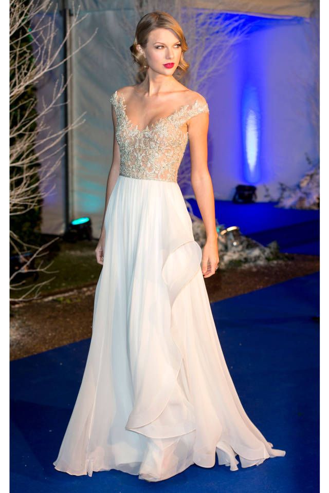 a woman in a white dress walking down a blue carpeted area with trees and lights behind her