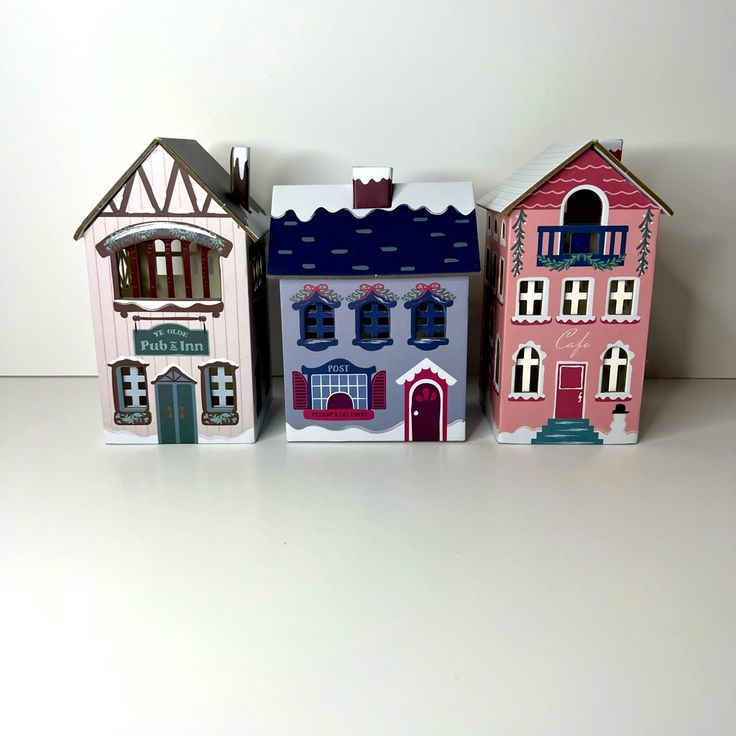 three little houses are sitting side by side on a white surface, one is pink and the other is blue