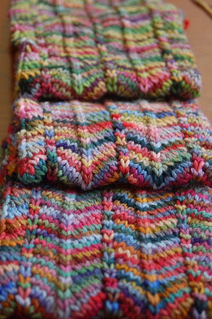 two multicolored crocheted pieces of cloth sitting on top of a wooden table