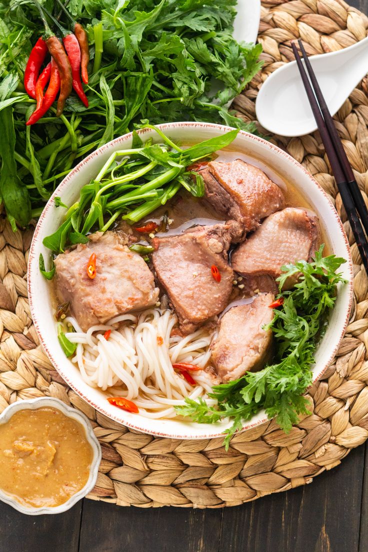 a bowl filled with meat and veggies next to dipping sauce on a table