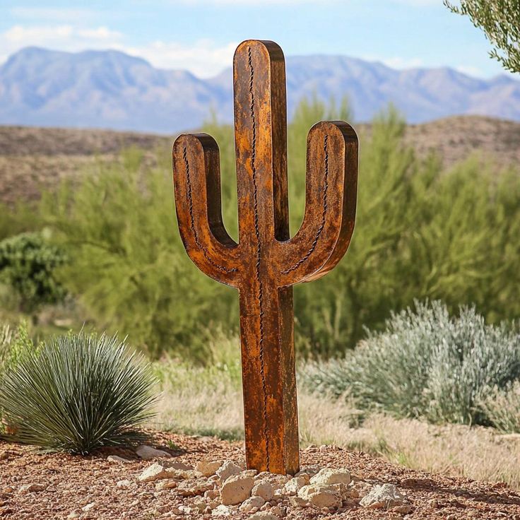 a large wooden cactus sitting on top of a dirt field next to a green bush